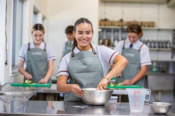 Students in a commercial kitchen preparing food, with one student mixing ingredients in a large metal bowl.